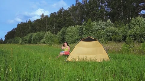 A tracking quadcopter flying through a tent where a woman is drinking tea with a Stock Footage 136745828