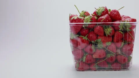 Tracking right across fresh red strawberries in plastic container on white backg 库存影片 334220608