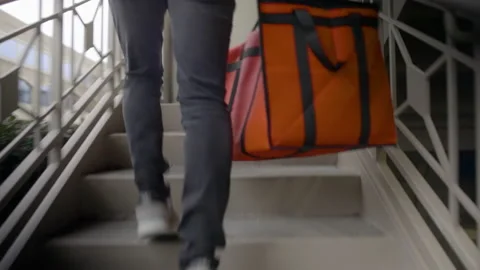 Tracking shot camera follows delivery person up steps delivering food with mask Stock Footage 145715454