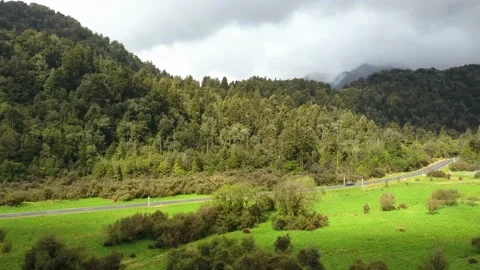 Tracking shot of car driving through lush green valley with mountains, drone 4k Video stock 147227408
