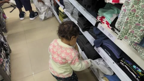 Tracking shot of a curious toddler crouching beside neatly stacked clothes in a Stock Footage 327388978
