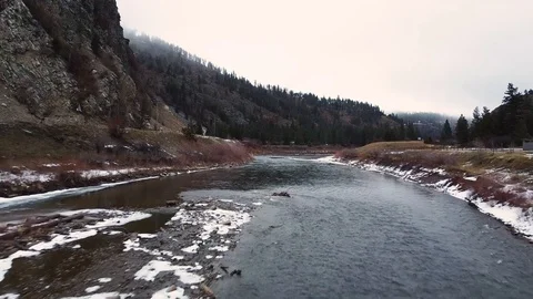 Tracking shot down a wide river with snow on bank and trees with overcast sky Stock Footage 125278016