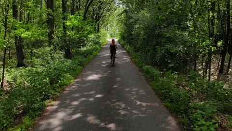 Tracking shot female cyclist from behind on paved road in forest Stock Footage 138757685
