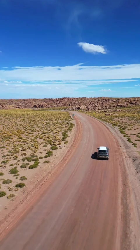 Tracking shot following car driving through curving dirt road past rocky Stockbeeldmateriaal 340990989