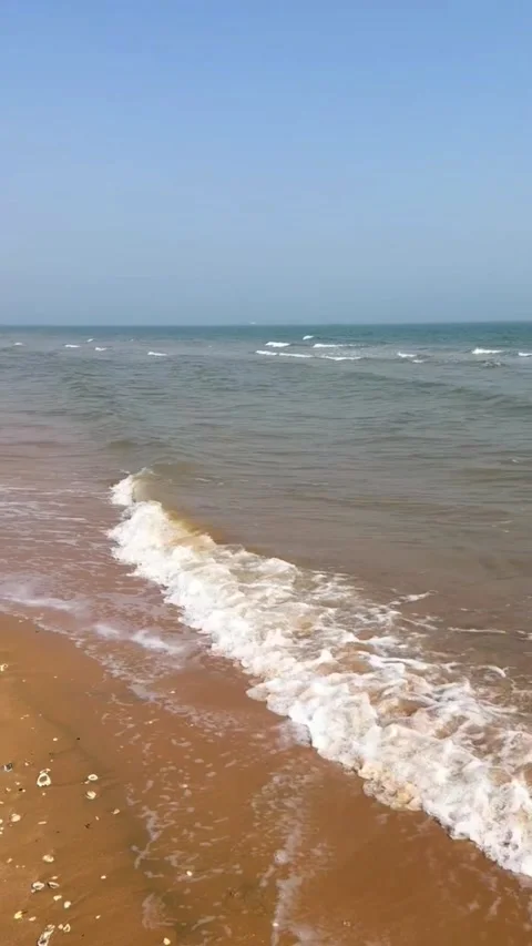 Tracking shot of gentle ocean waves rolling onto sandy beach at sunrise Stockbeeldmateriaal 333605252