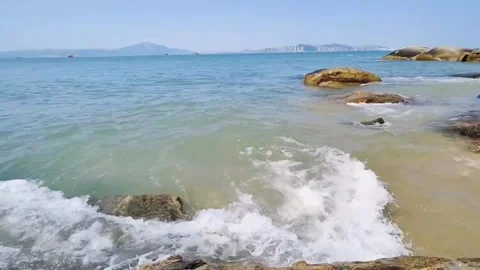 Tracking shot  gentle ocean waves lapping rocky shore in clear daylight Vidéo 333605304