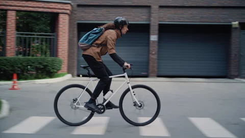 Tracking shot of guy with Helmet Rides Bicycle Along Greenery and Houses Stock-Footage 317562264