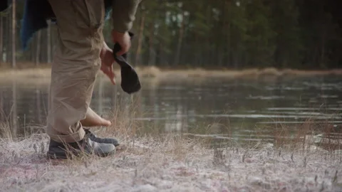TRACKING shot of an ice bather removing shoes and socks in front of frozen Video stock 166442153