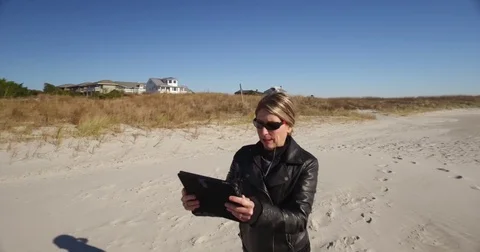 Tracking shot of lady using a tablet walking on the beach Stock Footage 71145730
