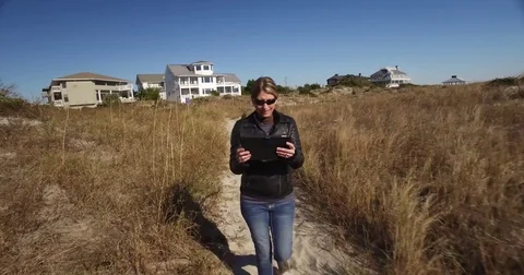 Tracking shot of lady walking through dunes on her tablet Stock Footage 71145697