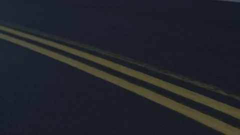 Tracking shot looking down on double yellow lines on dark wet pavement road Stock Footage 220312750