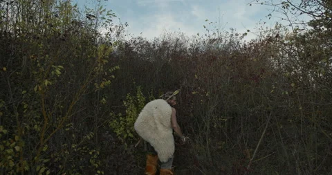 Tracking shot of man in animal hide walking through bushes while stalking prey Stock Footage 137982522