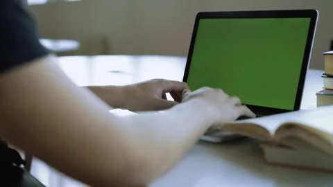 Tracking shot of a man with books typing on laptop with chroma key green screen Stock Footage