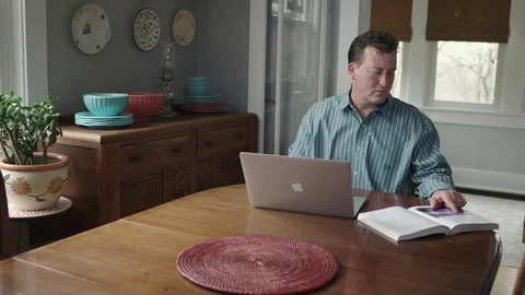 Tracking shot of middle aged man referring to book and using laptop Stock Footage 71341935