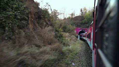 Tracking shot of a moving express train navigating through hills and entering a Stock Footage 336746519