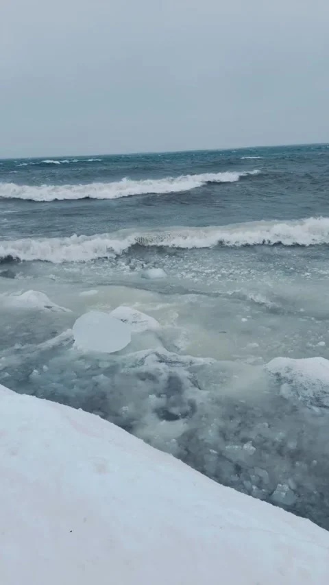 Tracking shot ocean waves crashing on snowy rocky shore in cold winter Vídeos de archivo 333605227