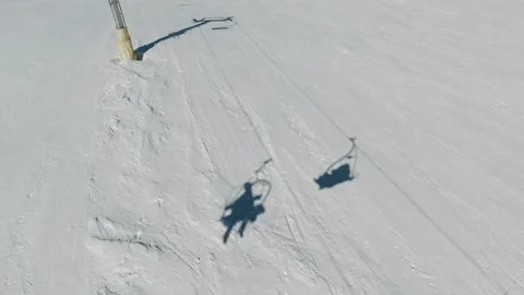 Tracking shot over packed snow as chairlift shadows glide across the slope Stock Footage 319797730