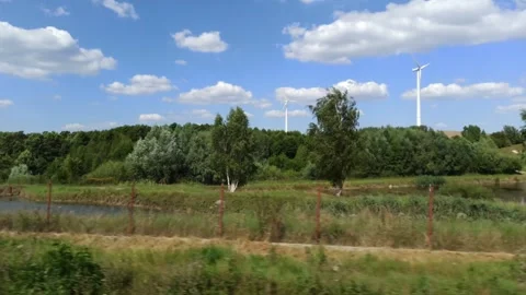 Tracking Shot Past Fields and Forest With Wind Turbines Beneath Partly Cloudy Stock Footage 337794022