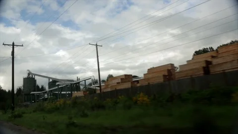 Tracking shot past piles of lumber and Lumber Mill. Stock Footage 86757573