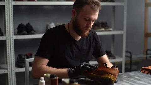 Tracking shot of shoemaker in black gloves rubbing paint on light brown leather Vídeos de archivo 150011975