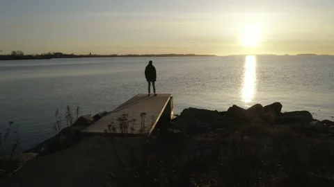 Tracking shot of a silhouetted man standing looking at sunrise over a lake Stock Footage 146293607