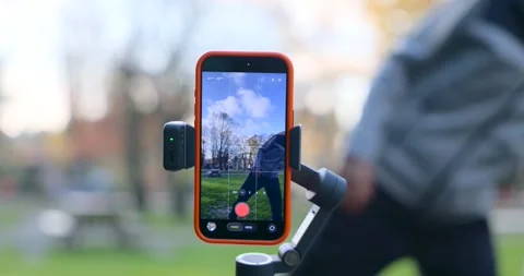 Tracking shot of a smartphone on a gimbal recording video in a park as a man Stock Footage 328601302