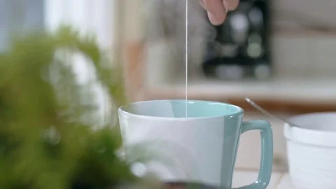 Tracking shot of tea bag bobbing in teal mug before hispanic man picks it up Stock Footage 84478016
