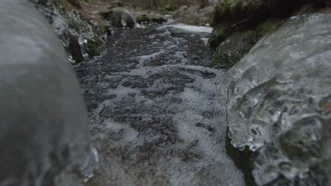 Tracking shot through frozen bubbling stream with small waterfall  Stock Footage 146278213
