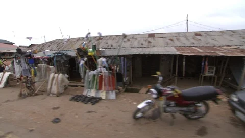Tracking shot through Lagos on dirt road, past tin-roofed shops. Stock Footage 86760925