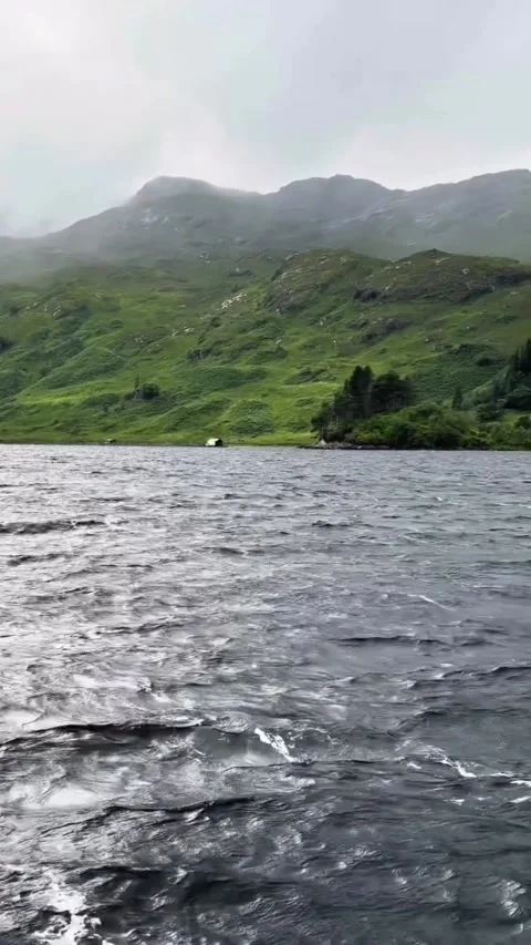 Tracking shot turbulent lake waves crashing against mountainous green landscape Vidéo 333605253