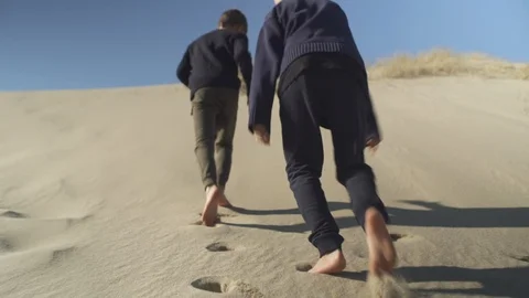 Tracking shot of two boys climbing a sand dune barefoot Vidéo 107613965