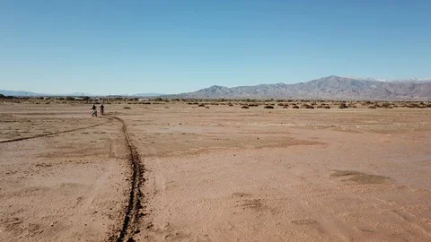 Tracking Shot of Two Motocross Bikers Riding in a Sandy and Muddy Desert Stockbeeldmateriaal 129409559