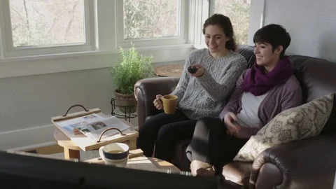 Tracking shot of two young ladies enjoying a program on television Stock Footage 70808998