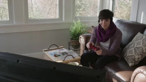 Tracking shot of a young lady gaming on a television in her sunroom Stock Footage 70809763