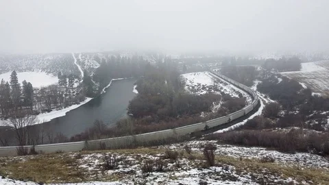 Tracking show over a train passing through snow covered valley along river Stock Footage 124616201