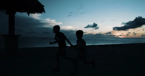 Tracking side  shot of two boys running on the beach while sun is almost set. Stock-Footage 98270997