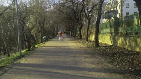 Tracking slow-motion shot of a young girl roller skating down a sunlit park Stock Footage 332567714