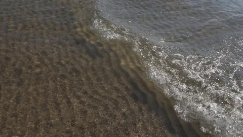 Tracking slow motion sunlit lake wave in shallow water. Rippled sand. Stock Footage