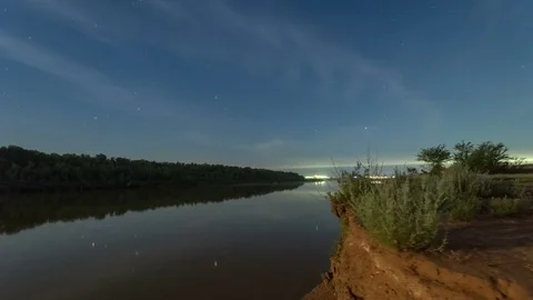Tracking time lapse of blue starry sky with flowing clouds reflecting in calm Stock Footage 75327096