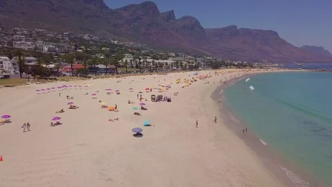 A tracking view over umbrellas and bathers along the coastline of Camps Bay. Stock Footage 83336885