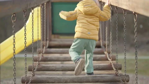 Tracking young kid carefully walk over hanging bridge on playground castle 4K Stock Footage 172030904