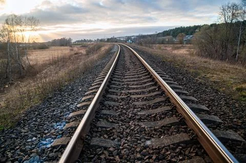 Tracks run straight through fields and trees with a sky full of clouds and ev Stock Photos