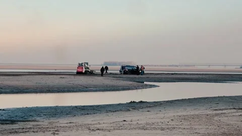 A tractor is actively attempting to pull out a car stuck in the soft Stock Footage 297254600