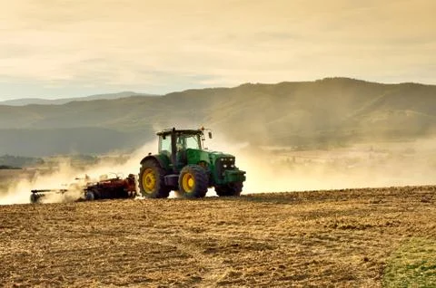 Tractor on agricultural field between forest and lake - scenery from spring,  Stock Photos