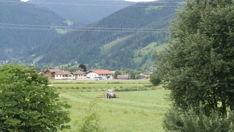 A tractor in an alpine meadow cutting green grass Stock Footage 158048061