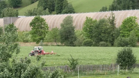 A tractor in an alpine meadow, a rake rakes the grass into rows for silage Stock Footage 158048052