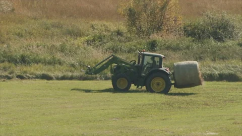 Tractor and ranch hand bring in round bales from hay field, 4k Stock-Footage 165703282