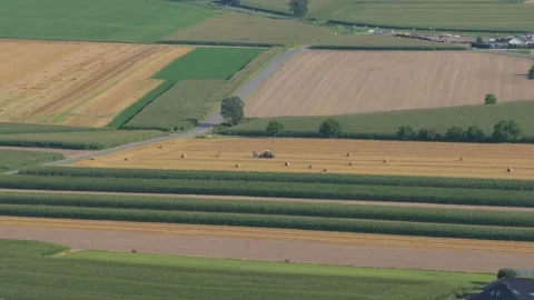 Tractor baling hay in vast patchwork countryside 스톡 동영상 348132525