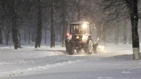 Tractor clears snow from road at night during heavy snowfall. Headlights Stock Footage 326749643