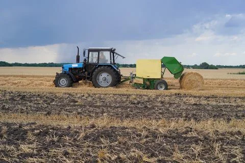 The tractor collects straw in a stack. Stock Photos